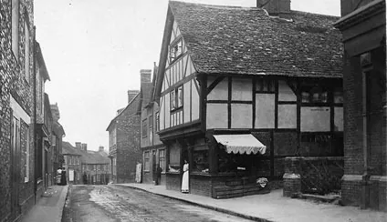 Old photograph of a narrow street with a timber-framed house and a shop awning