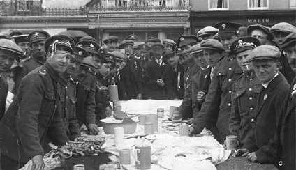 Old photograph of soldiers in caps and greatcoats gathered at a long table laid with food and mugs
